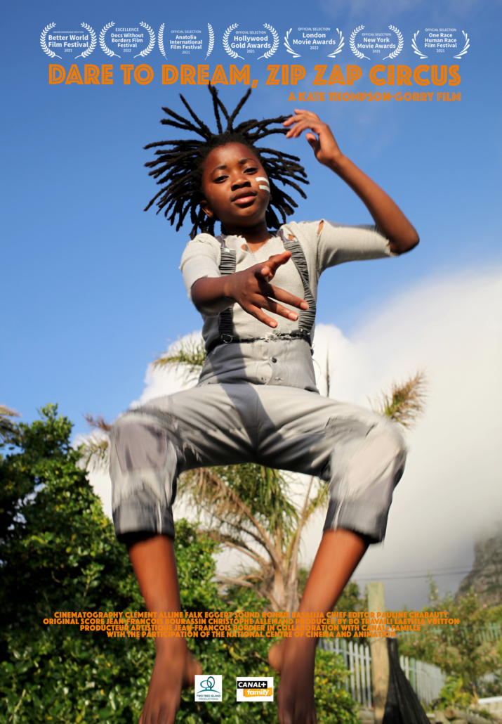 A child with dreadlocks and wearing grey overalls is captured mid-jump against a blue sky in this poster for the film “Dare to Dream, Zip Zap Circus." The text at the top displays the film’s title, while production details are listed at the bottom.