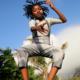 A child with dreadlocks and wearing grey overalls is captured mid-jump against a blue sky in this poster for the film “Dare to Dream, Zip Zap Circus." The text at the top displays the film’s title, while production details are listed at the bottom.